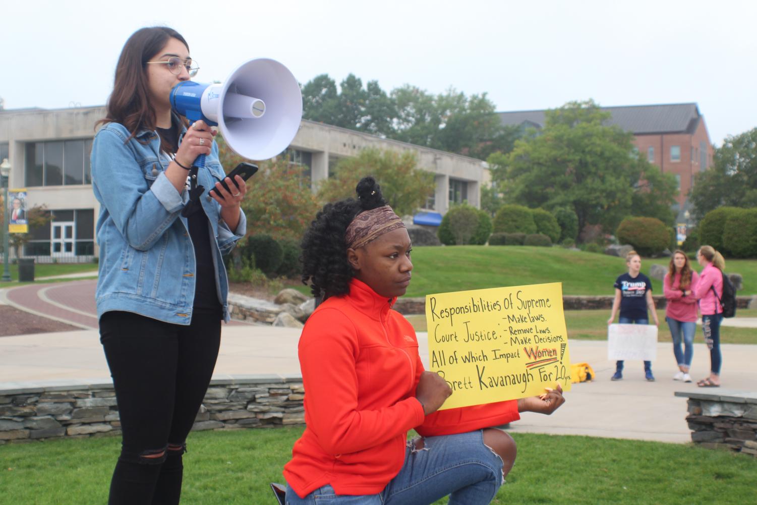 Anti-Kavanaugh protesters address the rally's crowd as a small group of Kavanaugh supporters stand in the distance.
